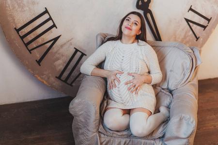 沉思怀孕的女人梦见孩子坐在扶手椅背后的巨大时钟照片