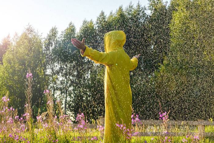 一个穿着黄色雨衣的人站在雨中向前看双手举向天空徒步旅行概念